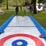 Curling Lane at a corporate fun day being enjoyed by colleagues with inflatables in the backgroubd