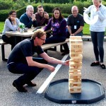 A group of people look on as a man plays on the Giant Jenga Hire