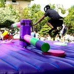 Guest at a corporate family fun day jumping over the sweeper arm of the inflatable wipeout challenge, on hire from Sunshine Events